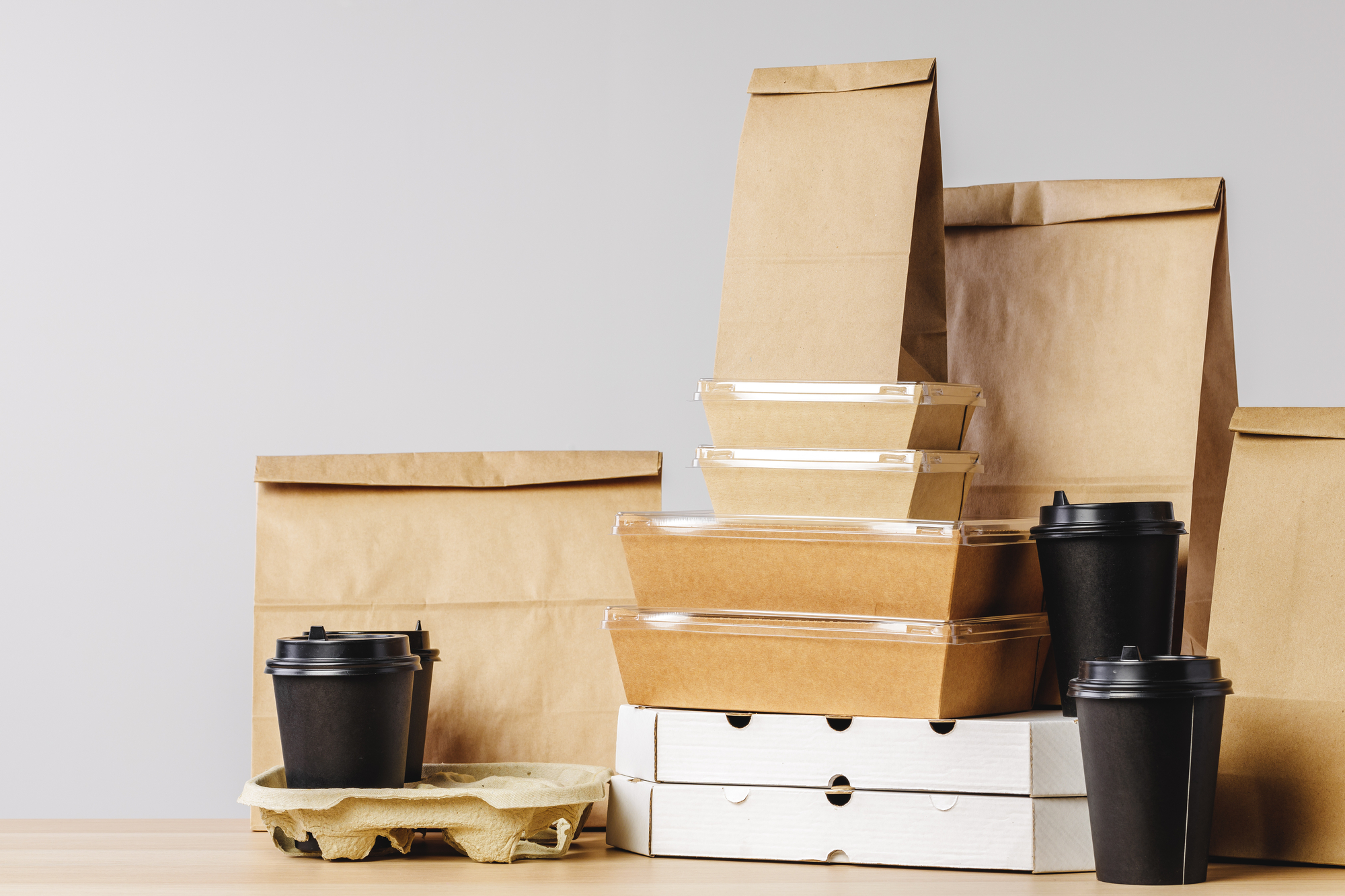 A collection of brown and white takeout containers and bags stacked against a grey background.